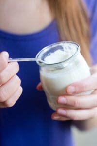 Person holding yogurt jar with spoon.