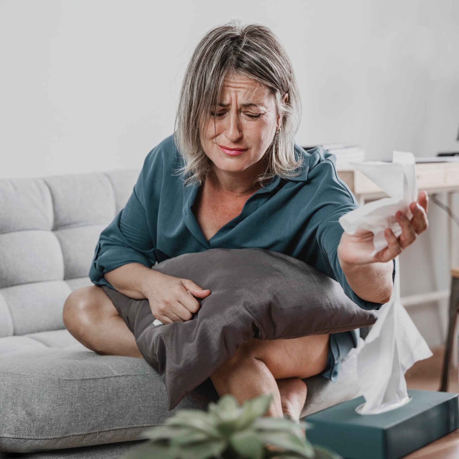 Woman feeling unwell holding tissues on couch.