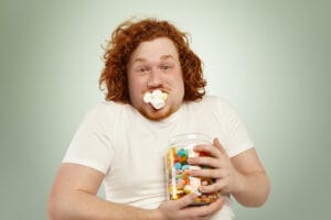 Person holding candy jar with marshmallows in mouth.