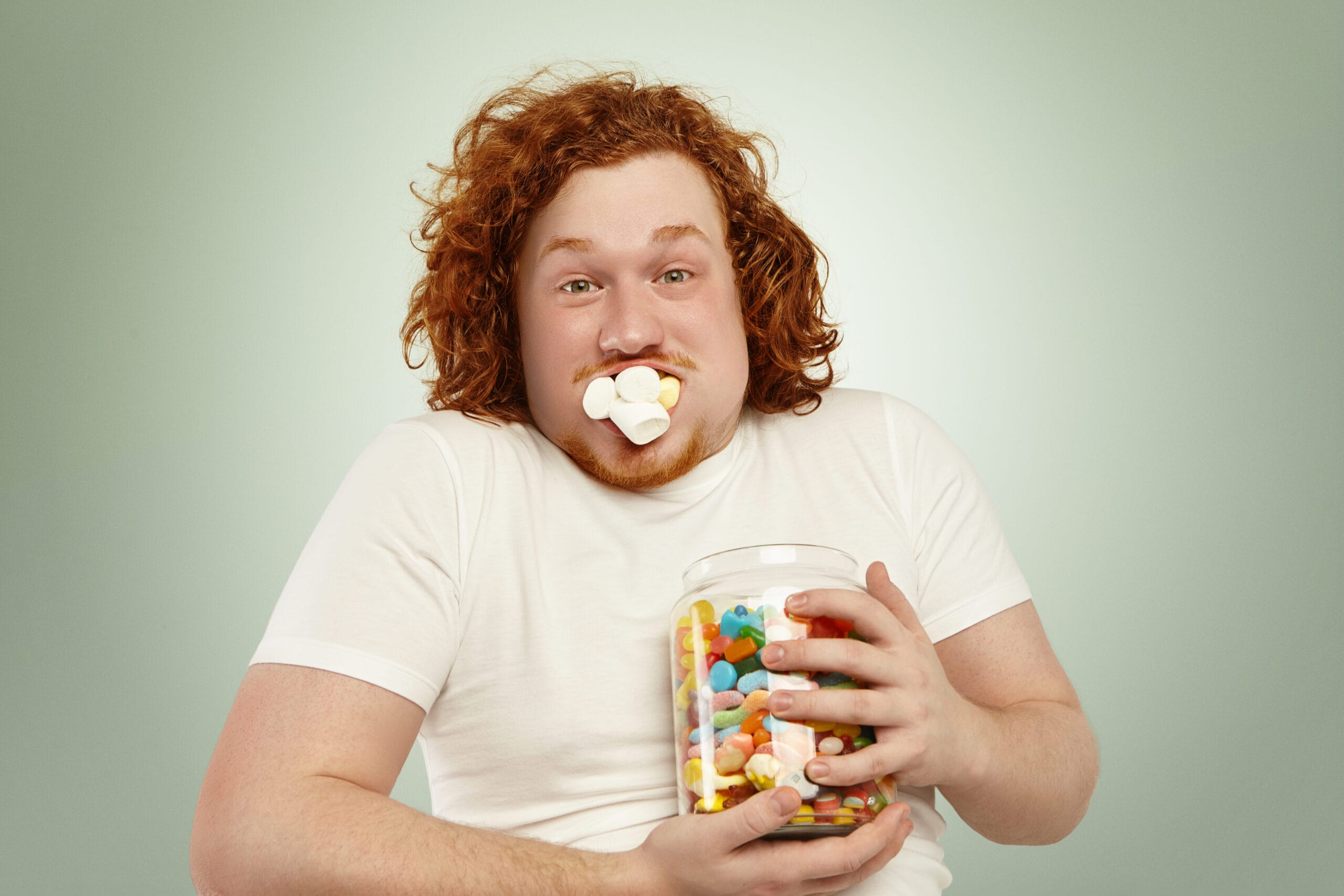 Person holding candy jar with marshmallows in mouth.