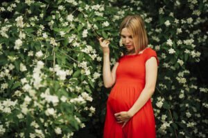 Pregnant woman in red dress among white flowers.
