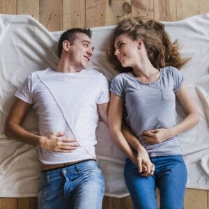 Couple lying on blanket, holding hands, smiling.